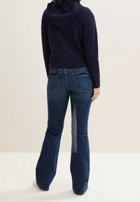 Námořnická mikina s kapucí, kombinovaná s tmavě modrými rozšířenými džíny s zadními kapsami a texturovaným denimovým povrchem.