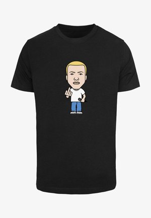 Must välja must T-särk, millel on joonistatud karikatuur, kellel on blondid juuksed, seljas valge särk ja sinised teksad, hoiab mikrofoni ja teeb käes žesti.