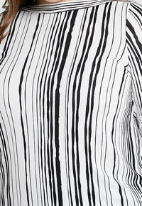 Zwart-witte top met verticale strepen, gemaakt van gladde stof. Heeft een ronde hals en een rechte silhouet, waarbij het streeppatroon wordt benadrukt.