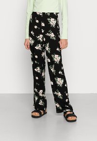 Calças florais pretas de corte largo, com flores brancas e rosas, combinadas com um top crop verde menta e sandálias de plataforma pretas.