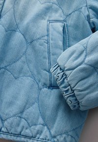 Svetlo modra prešita jakna z elastičnim manšetom in navpičnim stranskim žepom z vidnimi šivi.