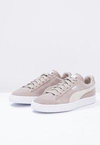 Graue Wildleder-Sneaker mit weißen Gummisohlen und Akzenten. Verfügt über ein einfaches Schnürsystem und Logodetails an der Seite und der Zunge.