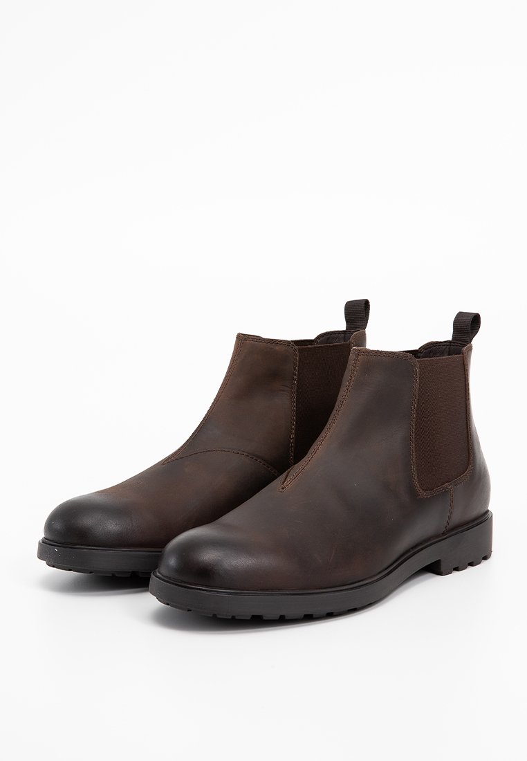 Bottines Chelsea en cuir marron avec des panneaux latéraux élastiques, bout arrondi, semelle en caoutchouc basse et accents foncés contrastants, arborant une texture lisse.