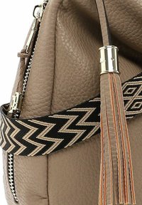 Taupe textured leather bag with black and beige zigzag woven strap and leather tassel with silver metal clasp.