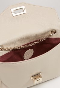 Beige nahkainen käsilaukku, jossa on kultaiset yksityiskohdat, ketjuyksityiskohta, teksturoitu pinta ja burgundy-värinen kangasvuori sisällä.