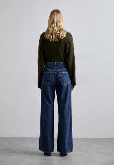 Bredde denimjeans i mørkeblå med høj talje, parret med en strikket olivengrøn sweater. Glat tekstur og afslappet design.