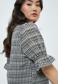 Blusa a righe grigie e bianche con maniche corte a sbuffo, dotata di polsini elasticizzati. Tessuto leggero con una vestibilità comoda.