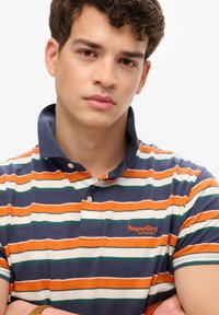 Gestreept poloshirt in marineblauw, oranje, groen en wit. Voorzien van een kraag met knopen en een geborduurd logo op de borst. Gemaakt van katoen.