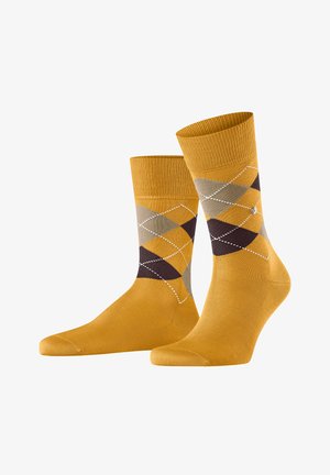 Chaussettes en coton jaune avec un motif argyle en marron, gris et crème, avec des contours blancs, un haut côtelé et une texture lisse.