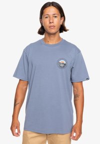 Light blue cotton t-shirt with short sleeves and a round neckline. Front features a circular graphic with mountains, waves, and sunset colors.