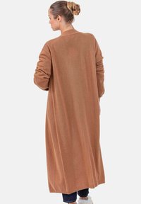 Langer, brauner Strickmantel aus weichem Stoff, mit langen Ärmeln und geradem Saum. Minimalistisches Design ohne sichtbare Verschlüsse.