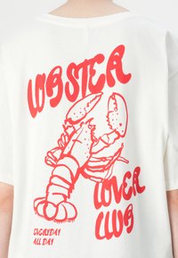 Hvid bomuld t-shirt med et stort rødt hummer grafik og teksten "LOBSTER LOVER CLUB" ovenfor, med "EVERYDAY ALL DAY" nedenfor.