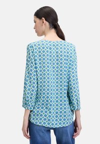 Blouse met blauw en groen patroon, met driekwart mouwen, ronde halslijn en zachte, lichtgewicht stof. Eenvoudig ontwerp aan de achterkant, rechte snit.