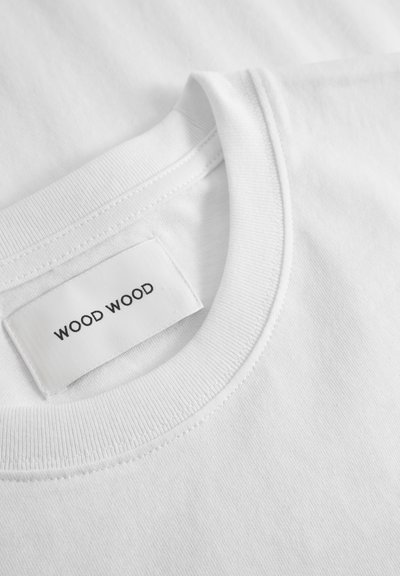 Balts kokvilnas T-krekls ar ribotu apaļu kakla izgriezumu, ar birku, kurā rakstīts "WOOD WOOD", kas iestrādāta iekšējā apkaklē. Gluda tekstūra.
