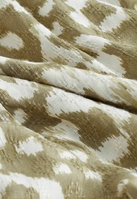 Tissu avec un motif ikat irrégulier en vert olive et blanc. La texture semble tissée avec des variations visibles dans le fil et la brillance.