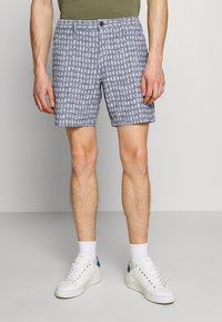Shorts en azul marino con un patrón geométrico blanco. Hechos de tejido ligero, cuentan con cierre de botón y bolsillos frontales.