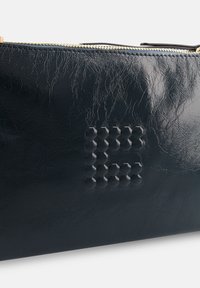 Pochette en cuir noir brillant avec un motif en nid d'abeille texturé et des détails de fermeture éclair dorée. Forme rectangulaire compacte.