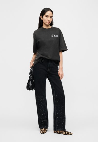 Μαύρο υπερμέγεθες t-shirt με λευκό λογότυπο, συνδυασμένο με μαύρο τζιν με διακοσμητικές καρφίτσες στο τελείωμα και παπούτσια με animal print. Μαύρη τσάντα χειρός.