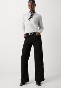 Light gray knitted sweater with a scoop neckline, paired with high-waisted black wide-leg pants and a black belt featuring a silver buckle.
