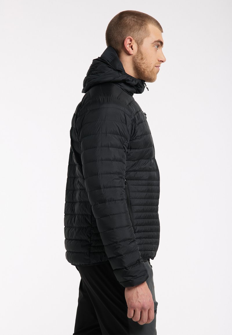 Chaqueta de plumas negra con capucha, con secciones acolchadas horizontales, bolsillos frontales con cremallera y puños elásticos para un ajuste ceñido.