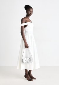 Abito bianco scollato sulle spalle con corpetto aderente e gonna a campana. Borsa a tracolla di metallo argento con design strutturato, abbinata a décolleté neri con cinturini.