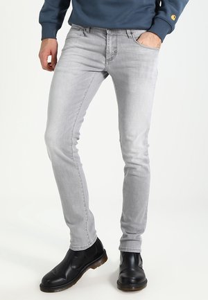 Schmal geschnittene, hellgraue Denim-Jeans mit einer glatten Textur. Getragen mit einem blauen Sweatshirt und schwarzen Stiefeletten mit elastischen Seiten.