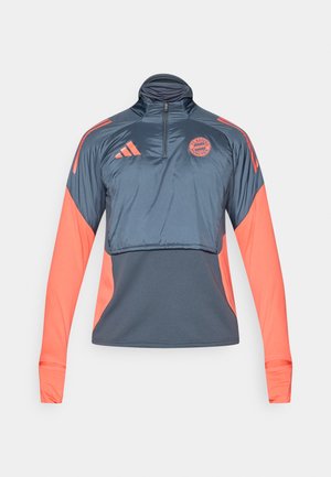 Pulover s polovičnim zadrgo iz gladkega, lahkega materiala. Ima temno modro telo s koralnimi rokavi in akcenti. Logotip na prsih. Dolgi rokavi.