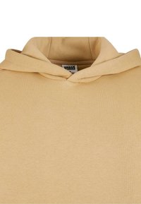 Sweat à capuche beige avec une capuche à double couche et une étiquette "Urban Classics" à l'intérieur de l'encolure.