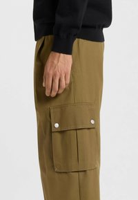 Cargo trousers in khaki fabric with a side pocket featuring silver snap buttons. Straight cut, smooth texture, and relaxed fit.