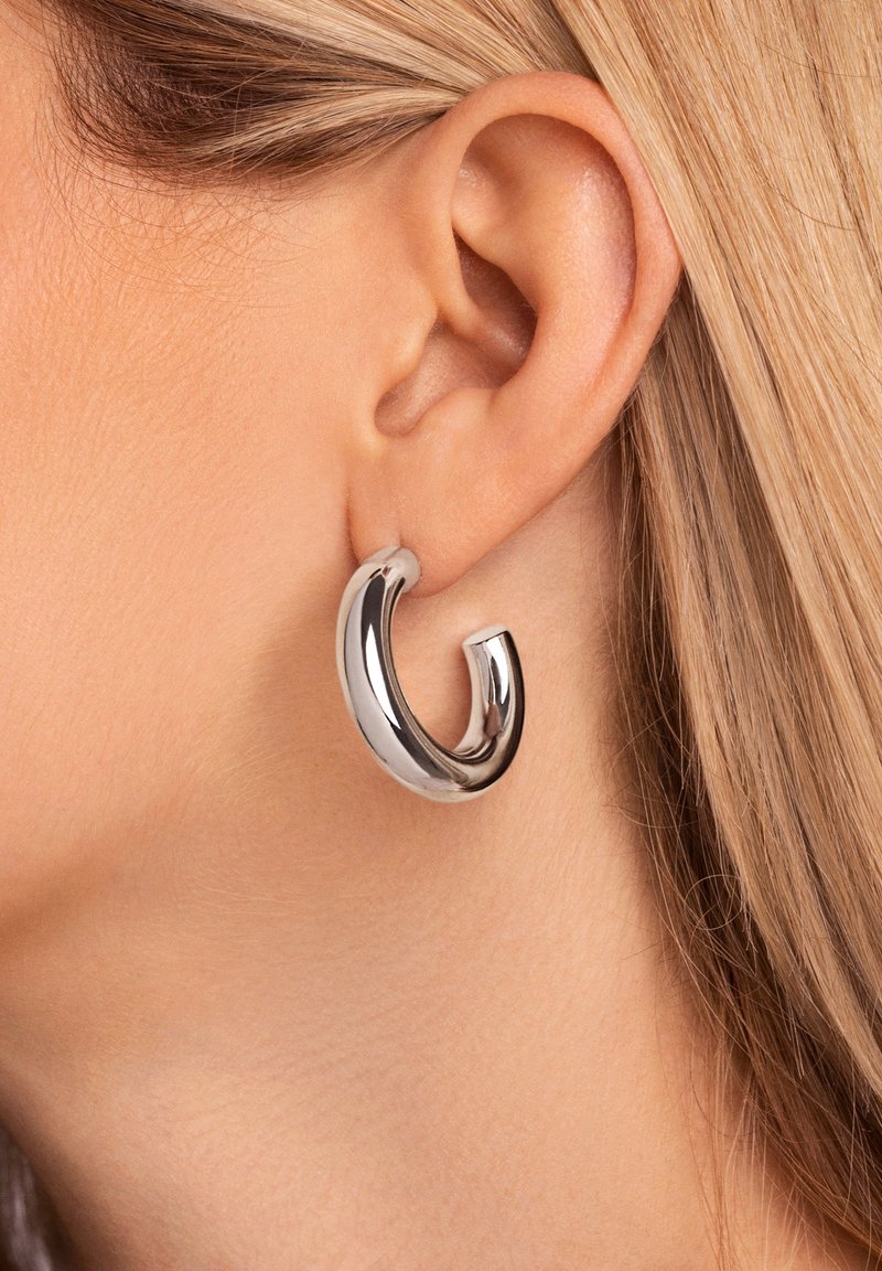 Orecchino a cerchio in argento con un design elegante e curvilineo. Presenta una finitura lucida e una forma unica e asimmetrica.