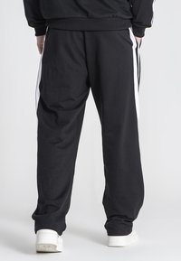 Sorte sweatpants lavet af blødt stof, med hvide sidelister, elastisk talje og en afslappet pasform. Enkel design og komfortabel stil.