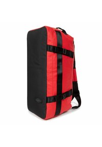 Sac de sport rouge et noir de forme rectangulaire, fabriqué en tissu durable, avec des sangles noires et un patch avec logo.