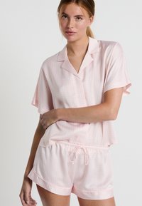 Pigiama a maniche corte di colore rosa chiaro in tessuto morbido con motivi circolari bianchi, composto da una maglietta con colletto e pantaloni corti con vita elastica.
