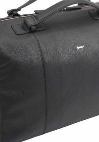 Serviette en cuir noir avec surface texturée, fermeture éclair et poignées courtes. Présente un petit logo métallique en accent sur le devant.