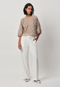 Beige strukturiertes Oberteil mit horizontalen Streifen, lockere Passform, kombiniert mit weißen, geraden Hosen und metallisch silbernen, spitzen Schuhen.