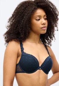 Σουτιέν σε ναυτικό μπλε με επένδυση, διακοσμητικό δαντελωτό τελείωμα, πουά σχέδιο και ρυθμιζόμενα λουράκια. Διαθέτει πλευρικό δίχτυ και κεντρικό διακοσμητικό κουμπί.