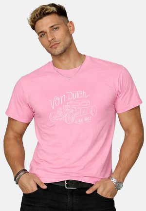Jeune homme aux cheveux courts et bouclés portant un t-shirt rose Von Dutch avec un motif de voiture vintage et le texte « Live Fast ».
