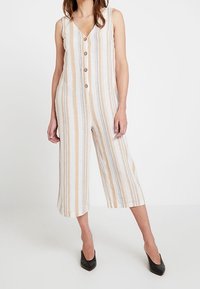 Striped jumpsuit in beige, cream, and light blue. Features a V-neck, button front, sleeveless design, and cropped wide legs.