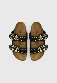 Sorte ruskindssandaler med to justerbare remme, der har guldbukler og nitteaccenter. Korkfod og åben tå-design.