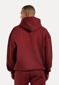 Sudadera burdeos con una capucha amplia, hombros caídos y puños acanalados. Fabricada con un material suave de textura lisa.
