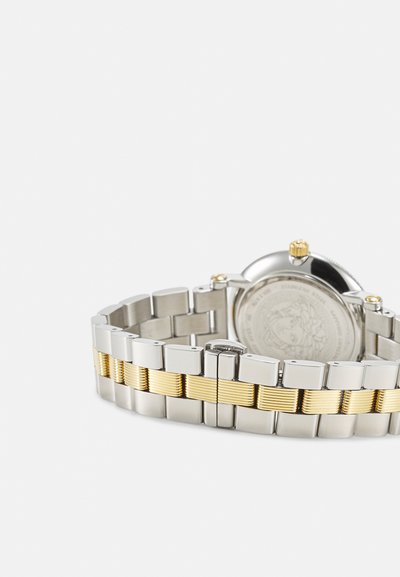 Nerūdijančio plieno laikrodis su sidabrine ir auksine tekstūruota apyranke, apvaliu korpusu ir karūnėle. Gale yra išgraviruoti detalės.