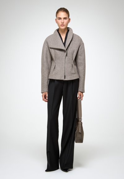 Chaqueta de lana gris con un collar ancho, cremallera asimétrica y corte holgado, combinada con pantalones de pierna ancha negros y un bolso gris.