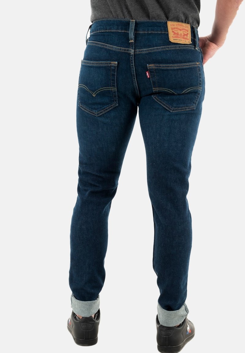 Schmal geschnittene Jeans in Dunkelblau mit einem markanten Design der Gesäßtaschen und einem Lederpatch am Bund. Mit umgeschlagenen Knöcheln.