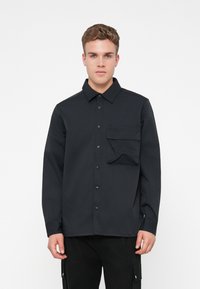 Zwarte lange mouwen shirt met een knoopsluiting, voorzien van een borstzak aan de voorkant en een gestructureerde kraag, gemaakt van een gladde stof.