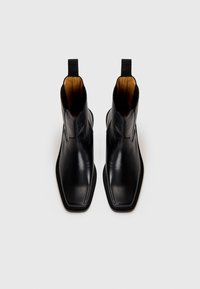 Bottes noires en cuir à talons, avec un design à bout pointu. Elles présentent une finition lisse, des accents cousus, et des languettes à l'arrière pour un enfilage facile.