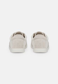 Deux baskets en suede beige clair avec un profil bas, un bout rond et un design minimaliste. Côtés texturés et doublure en textile doux.
