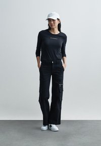 Langermet svart genser med hvit logo, svarte cargobukser med lommer og hvite joggesko. Komplettert med en hvit caps.