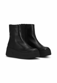 Crne kožne gležnjače s elegantnim dizajnom, sa bočnim patent zatvaračem i debelim platformskim potplatom. Glatka tekstura i zaobljeni oblik prsta.