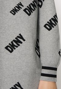 Pull gris avec motif du logo "DKNY" en tricot noir, poignets côtelés à rayures noir et blanc, et texture douce.