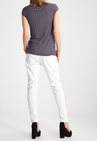 Niebieski, wzorzysty top z krótkim rękawem w połączeniu z dopasowanymi białymi spodniami i czarnymi szpilkami. Strój wyróżnia się subtelnym geometrycznym wzornictwem.